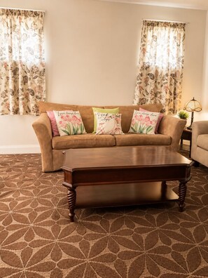 A living room with a brown sofa, floral cushions, a wooden coffee table, and a patterned carpet.
