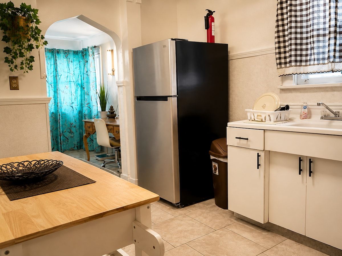 A kitchen with a stainless steel refrigerator, a sink with a faucet, and a trash bin.