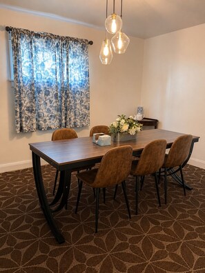 Un coin repas comprenant une table rectangulaire, six chaises, un vase avec des fleurs et un luminaire suspendu.