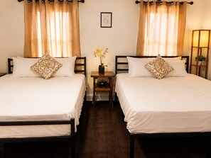 Une chambre d’hôtel avec deux lits simples, une petite table sur laquelle est posé un vase de fleurs et une lampe sur une table de chevet.