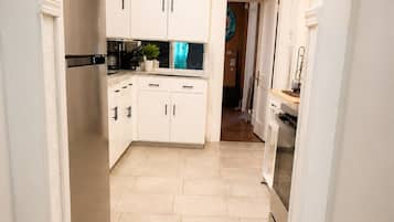 A narrow hallway leading to a kitchen with white cabinets, a refrigerator, and a stove.