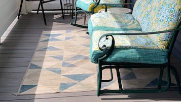 A covered outdoor seating area with a sofa and chairs, a patterned rug, and a view of a house in the background.