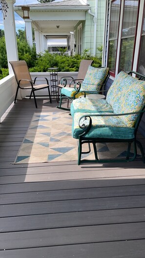A covered outdoor seating area with a sofa and chairs, a patterned rug, and a view of a house in the background.