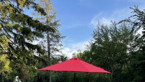 Une terrasse extérieure avec une table et des chaises, un parasol rouge et une clôture en treillis métallique.