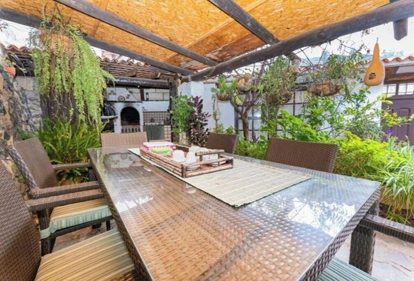 Relax in the serene outdoor patio surrounded by lush greenery and a traditional building in the background.