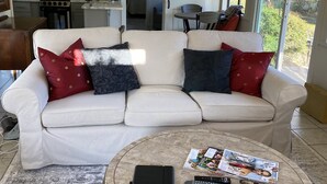 Ein Wohnzimmer mit einem weißen Sofa, einem runden Couchtisch und einer Küche im Hintergrund.