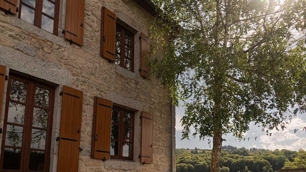 Un edificio de piedra con contraventanas de madera y una mesa de picnic.