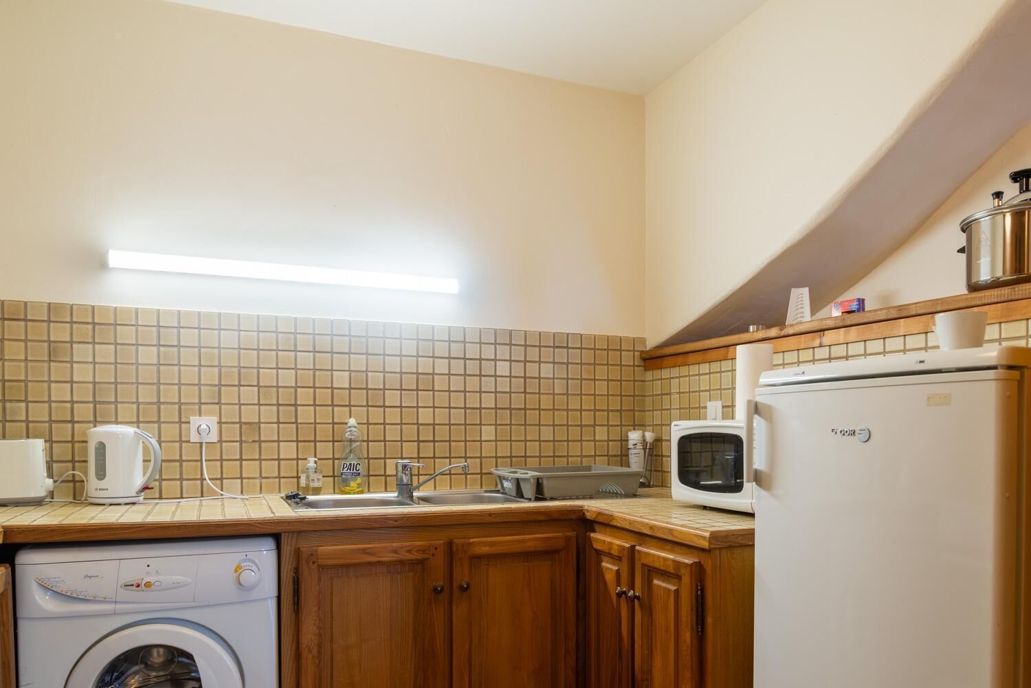Een kleine keuken met een wasmachine, magnetron en spoelbak.