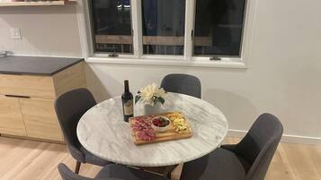 A round marble table with four chairs, a bottle of wine, a floral centerpiece, and a charcuterie board.