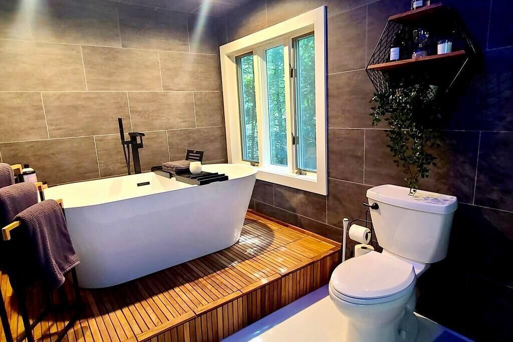 A modern bathroom with a freestanding bathtub, a toilet, and a window providing natural light.