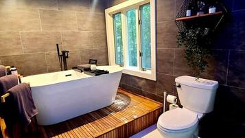 A modern bathroom with a freestanding bathtub, a toilet, and a window providing natural light.