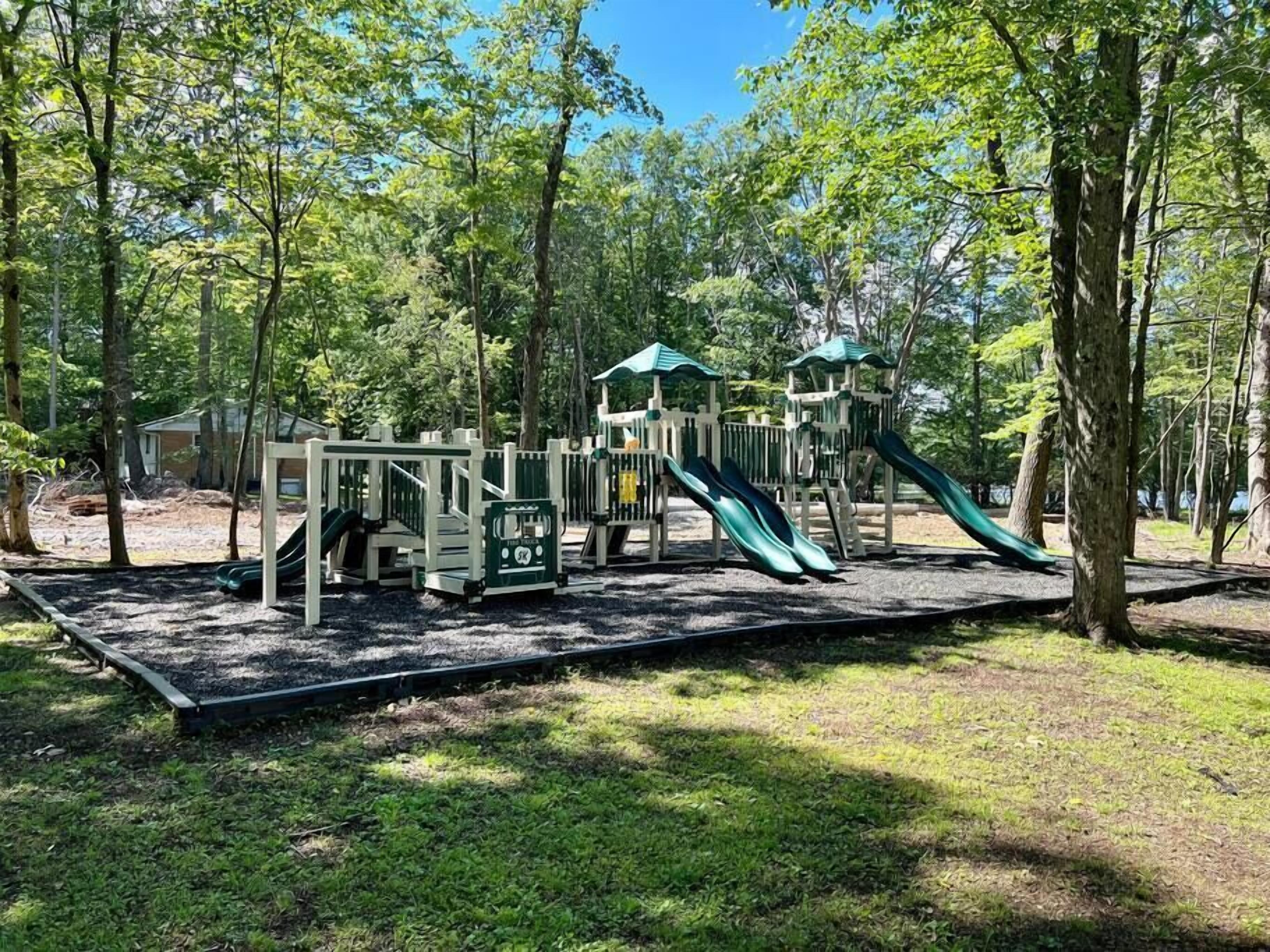 A playground with slides and climbing structures surrounded by trees.