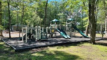 A playground with slides and climbing structures surrounded by trees.