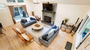 Amplia sala de estar con chimenea, un sofá, una mesa de centro y un televisor montado en la pared.