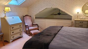 Un dormitorio con techo inclinado, cama, cómoda, silla y espejo.