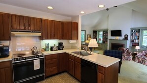 A modern kitchen with wooden cabinets, a built-in oven, and a dishwasher. There is a dining area with a floral sofa and a fireplace. -  Dog friendly lakefront home w/fireplace near Lk George. Telecommuters welcome! (Fort Ann)