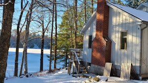 A cabin with a wooden exterior, a brick chimney, and a small deck. -  Dog friendly lakefront home w/fireplace near Lk George. Telecommuters welcome! (Fort Ann)
