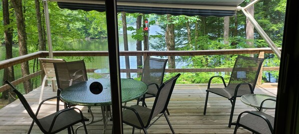 A covered outdoor deck with a table and chairs, overlooking a lake surrounded by trees. -  Dog friendly lakefront home w/fireplace near Lk George. Telecommuters welcome! (Fort Ann)