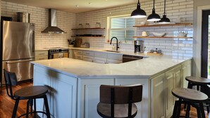 Une cuisine moderne dotée d’un îlot central, d’appareils électroménagers en acier inoxydable et de luminaires suspendus.