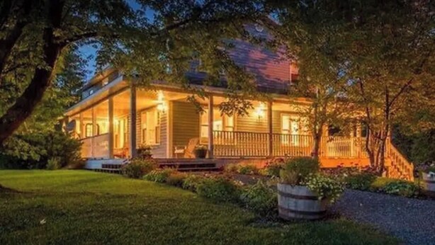 Une maison à deux étages avec un porche, entourée d’arbres et d’une pelouse bien entretenue.