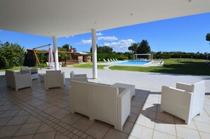 Un espace extérieur aménagé en terrasse, avec des meubles en osier blanc, une piscine et une pelouse bien entretenue.