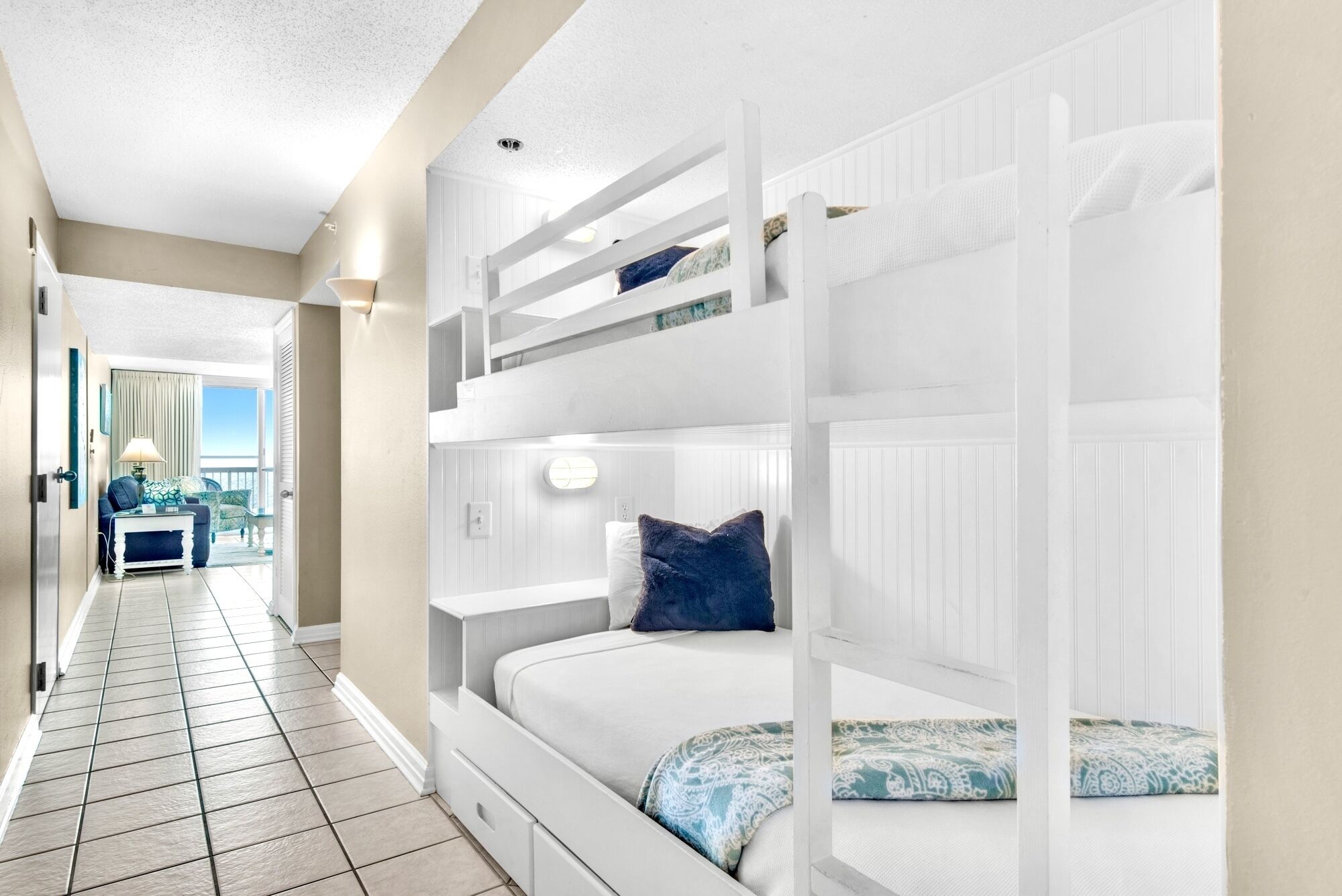 A hotel room with a bunk bed, a small desk with a lamp, and a view of the balcony.