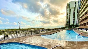 Et poolområde med flere swimmingpools, en sandstrand og en høj bygning i baggrunden.