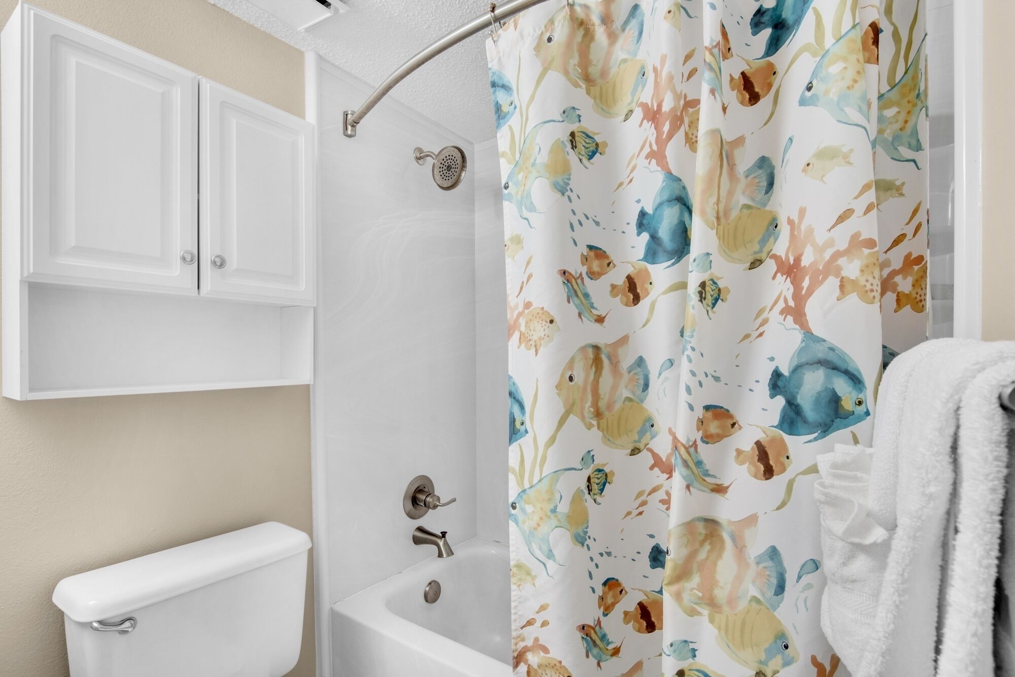 Une salle de bain équipée de toilettes, d’une baignoire et d’un rideau de douche orné d’un motif de poissons.