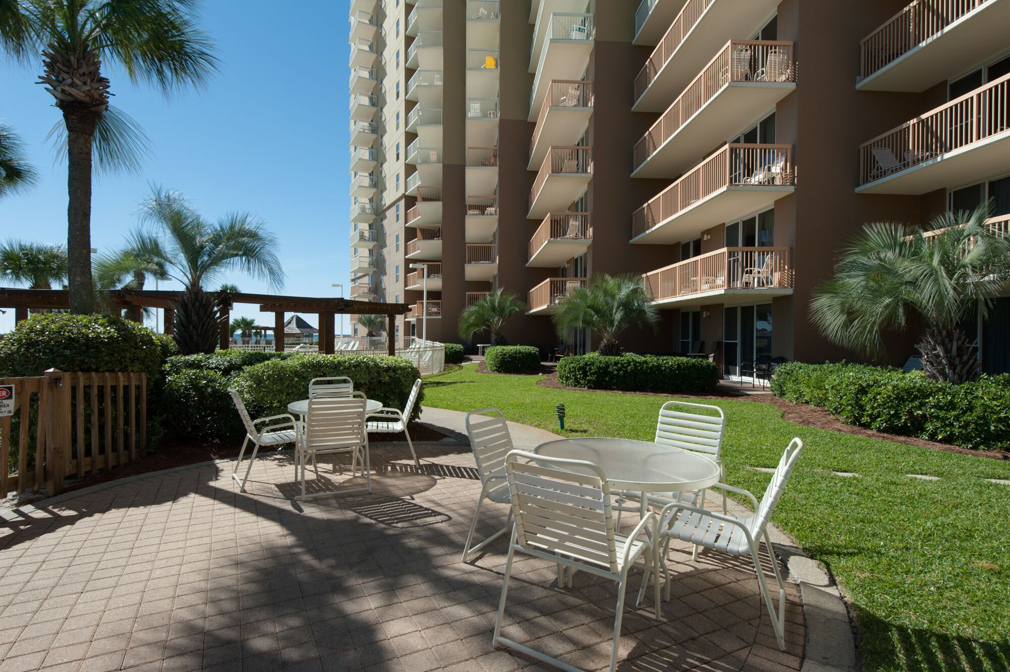 A courtyard with outdoor seating, palm trees, and a multi-story building with balconies.