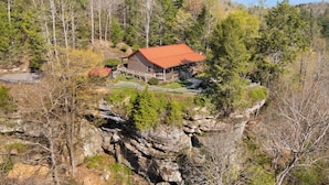 Une cabane avec un toit rouge, entourée d’une forêt dense et d’un terrain rocheux.