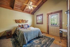 A bedroom with a wooden ceiling, a bed with a striped bedspread, a small side table, a rug, a door with a window, and a ceiling fan. - Just 1 mile from Natural Bridge State Park! (Slade)