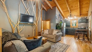 A cozy living room with a sofa, a coffee table, and a TV mounted on a wall with a wooden ceiling. - Under 1 mile from Natural Bridge State Park! (Slade)