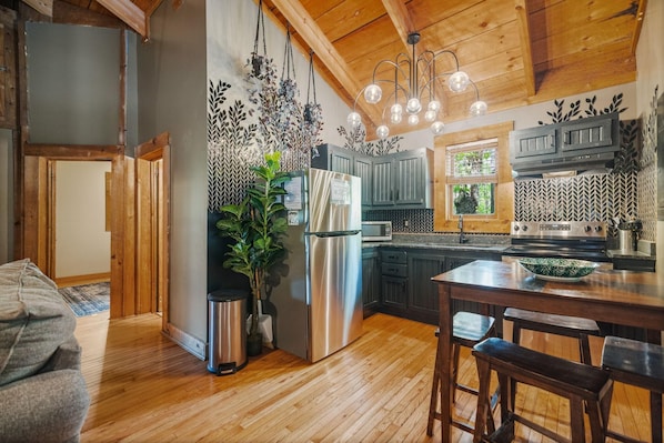 A kitchen with wooden cabinets, a stainless steel refrigerator, a microwave, and a wooden dining table with bar stools. - Just 1 mile from Natural Bridge State Park! (Slade)