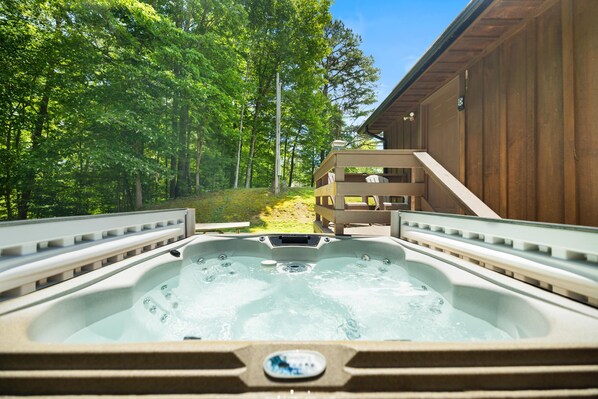 A hot tub with a wooden deck and a view of a forested area. - Quaint, cozy vacation cabin with hot tub near Natural Bridge State Park (Rogers)