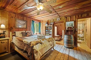 A rustic wooden room with a bed, a bookshelf, a desk, and a large barrel. - Quaint, cozy vacation cabin with hot tub near Natural Bridge State Park (Rogers)