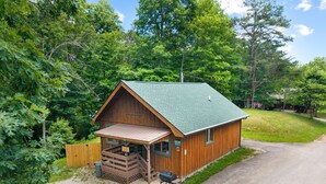 A wooden cabin with a porch, a gravel driveway, and a green roof. - Quaint, cozy vacation cabin with hot tub near Natural Bridge State Park (Rogers)