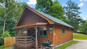 A wooden cabin with a porch, a barbecue grill, and a sign indicating a restaurant. - Quaint, cozy vacation cabin with hot tub near Natural Bridge State Park (Rogers)