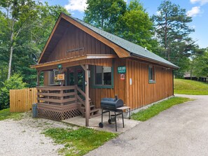 A wooden cabin with a porch, a barbecue grill, and a sign indicating a restaurant. - Quaint, cozy vacation cabin with hot tub near Natural Bridge State Park (Rogers)