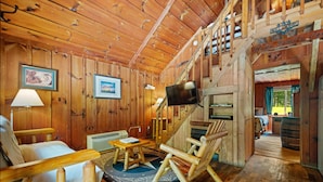 A wooden interior with a sofa, chairs, a television, and a staircase. - Quaint, cozy vacation cabin with hot tub near Natural Bridge State Park (Rogers)