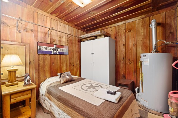 A wooden room with a bed, a heater, and a sign that says 'LIVE FREE RIDE HARD'. - Quaint, cozy vacation cabin with hot tub near Natural Bridge State Park (Rogers)