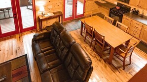 Ein gemütliches Blockhaus-Interieur mit Holzbalkendecke, einem Ledersofa, einem Esstisch mit Stühlen und einer Küchenzeile.