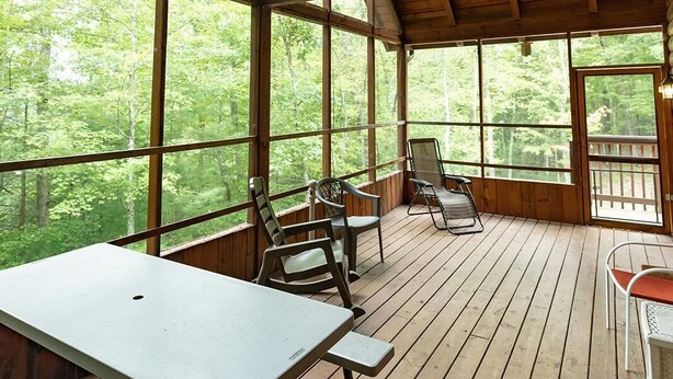 Eine Holzterrasse mit Tisch und Stühlen, großen Fenstern und einem Deckenventilator.