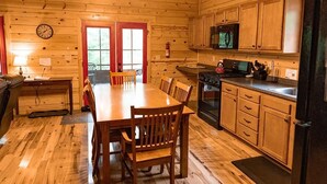 Ein Holzblockhaus-Innenraum mit Esstisch, Stühlen, einer Küche inklusive Geräte und einem Deckenventilator.