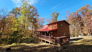 Eine Holzhütte mit Veranda und Terrasse, umgeben von Bäumen im Herbstlaub.