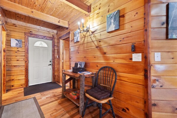 A wooden cabin interior with a door, a table with books, a chair, and a chandelier. - Secluded, Cozy Cabin with Hot Tub in a heavily forested setting. Great Location. (Rogers)