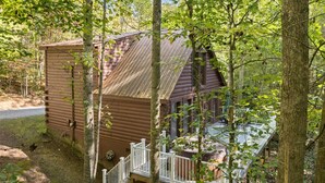 Una baita di legno con veranda e piccolo portico, immersa tra gli alberi.