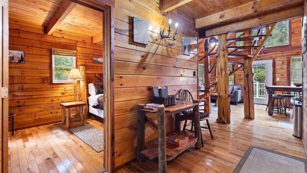 Interno accogliente di una baita in legno rustica, con una zona giorno confortevole, un tavolo da pranzo e una scala che conduce a un piano superiore.