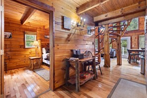 A rustic wooden cabin interior with a cozy living area, a dining table, and a staircase leading to an upper level. - Secluded, Cozy Cabin with Hot Tub in a heavily forested setting. Great Location. (Rogers)