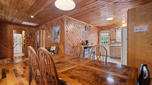 A wooden interior with a dining area, kitchen, and a sign that reads "GATHER RELAX".