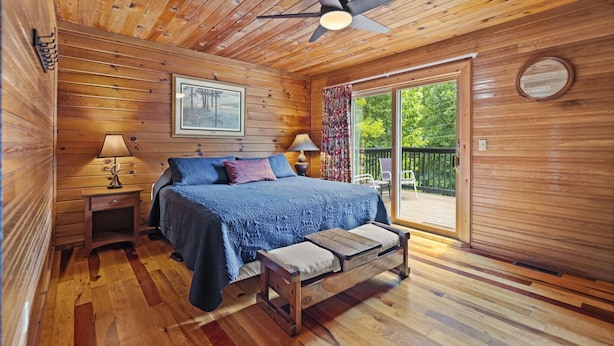 Een houten slaapkamer met een bed, een bankje, twee nachtkastjes, een plafondventilator en een grote schuifdeur naar een terras.